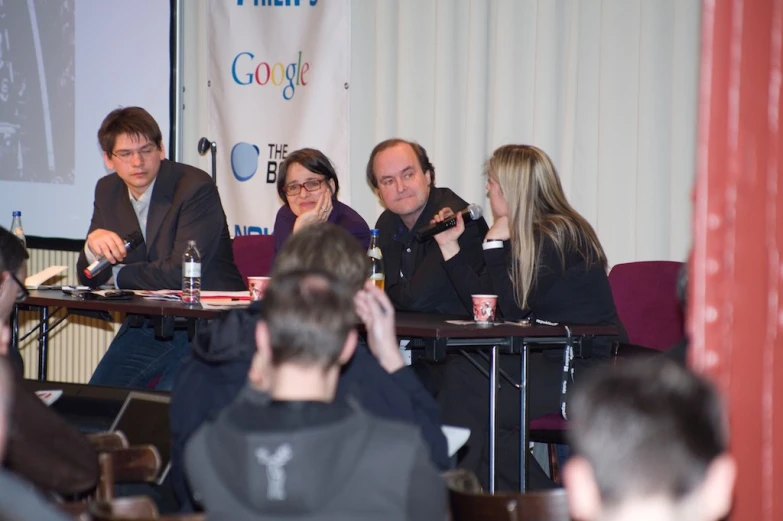 people at tables in front of a man on the screen