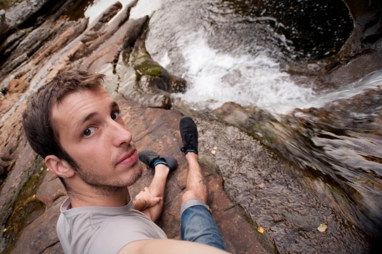 a man taking a selfie with his camera near a stream