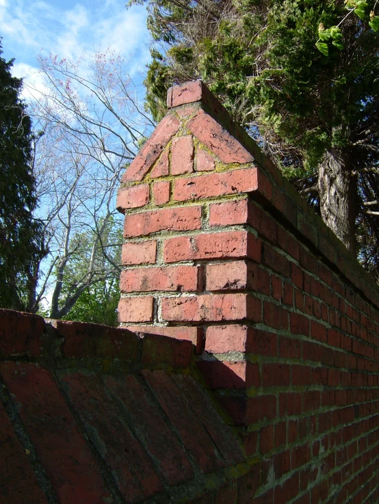 a red brick wall and some trees and clouds