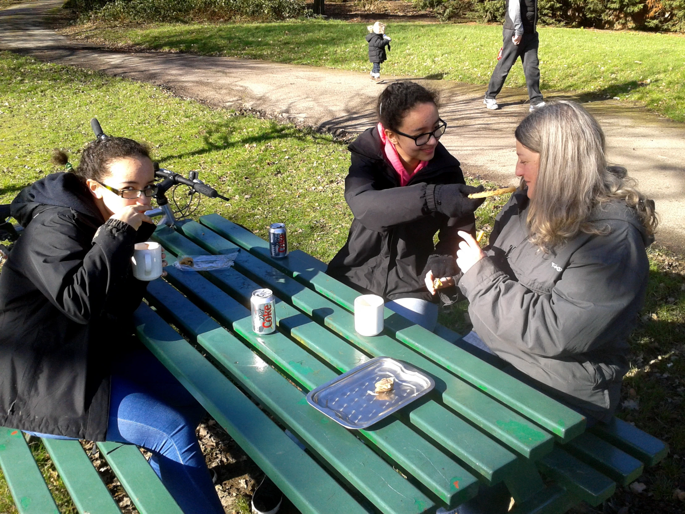 three people sit around a picnic table eating food