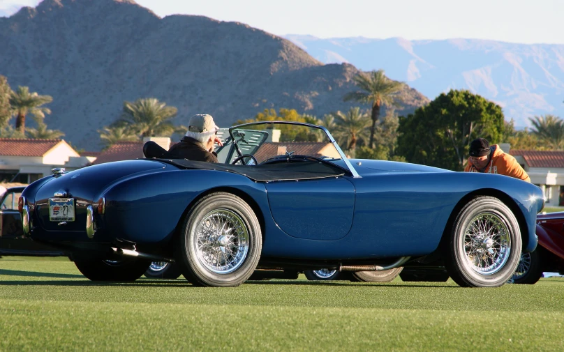 an older man is sitting in a large blue sports car