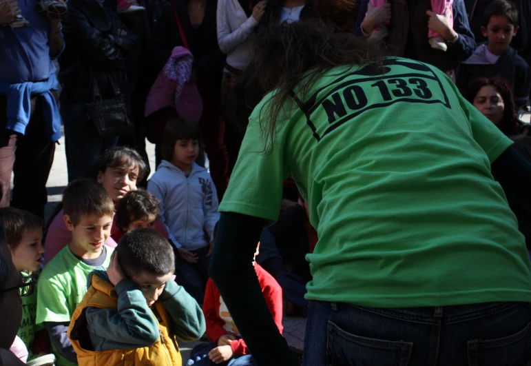 a man wearing a green shirt standing in front of a crowd of young children