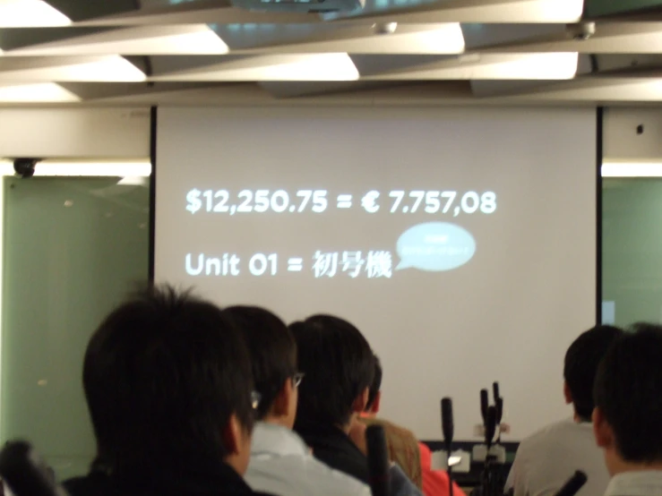 people in a conference room are watching an electronic message