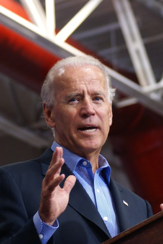 joe biden speaking from a podium with his hands in the air