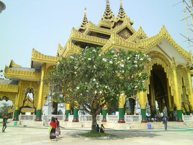 people walk past an ornate building and tree