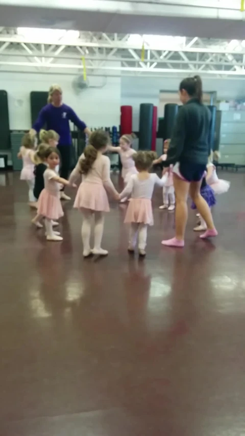 several girls dance in a large room with adults and children