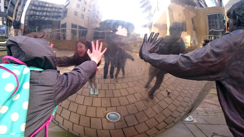 a woman with her hand up standing in front of a giant mirror