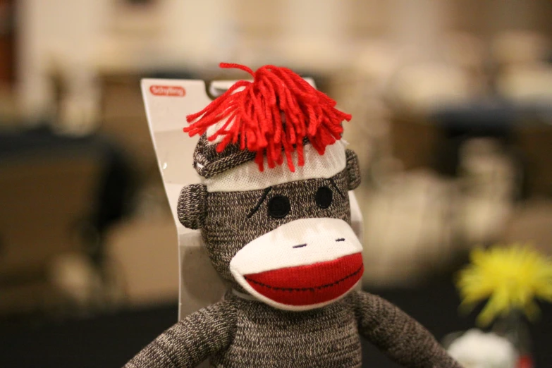 a sock monkey with a knitted hat and red hair sits beside a remote control