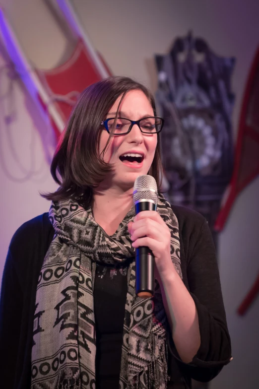 a woman wearing glasses standing with a microphone