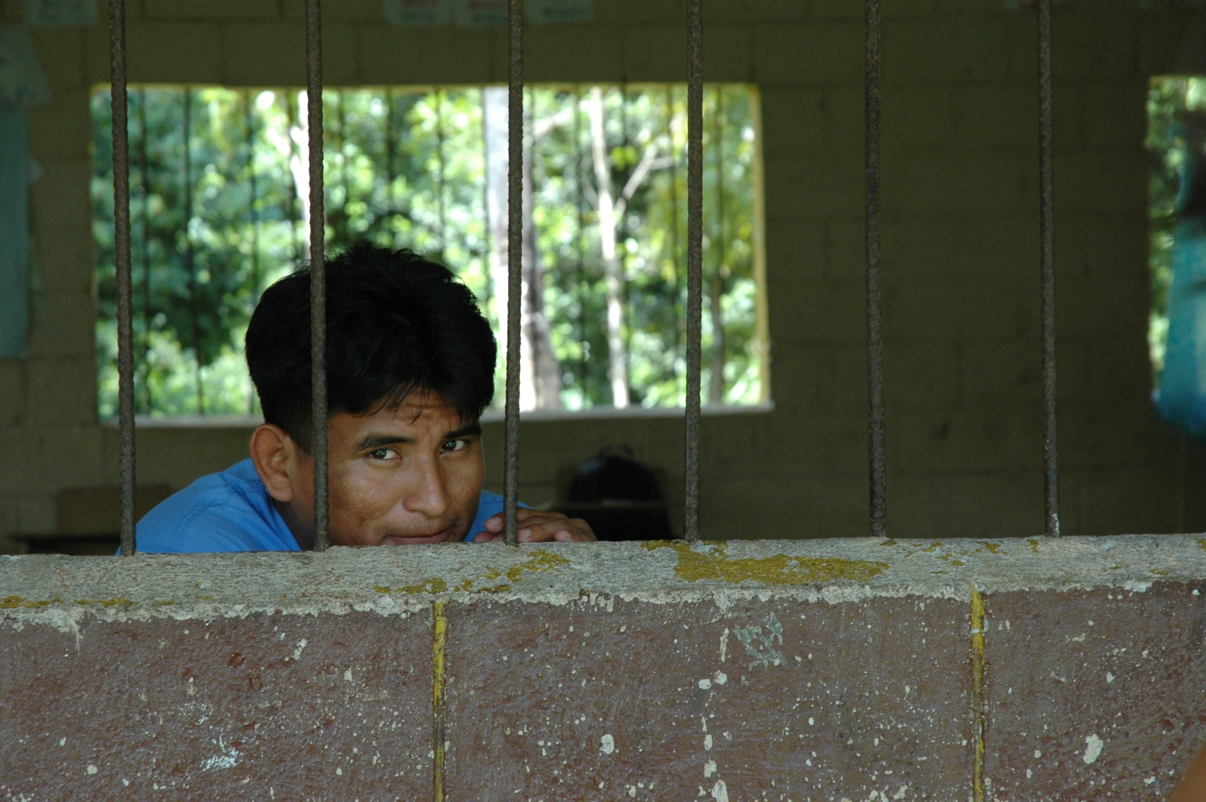 boy peering from prison behind bars with trees in background