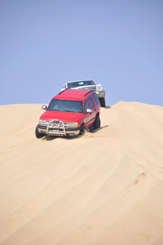 two jeeps riding in the sand in the desert