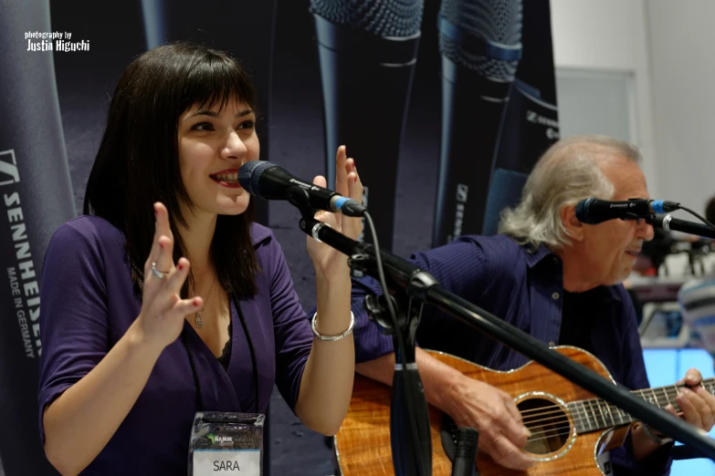 a woman singing into a microphone next to a man holding a guitar