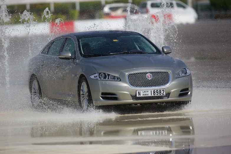 jaguar cars drive through an open street with lots of water splashing on them