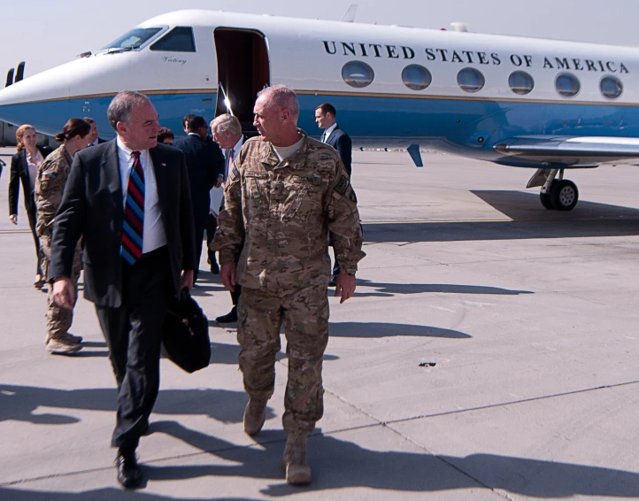 two men in military attire walk towards a jet