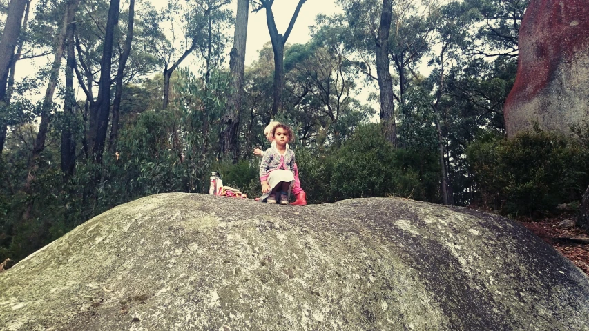 a little girl sitting on top of a large rock