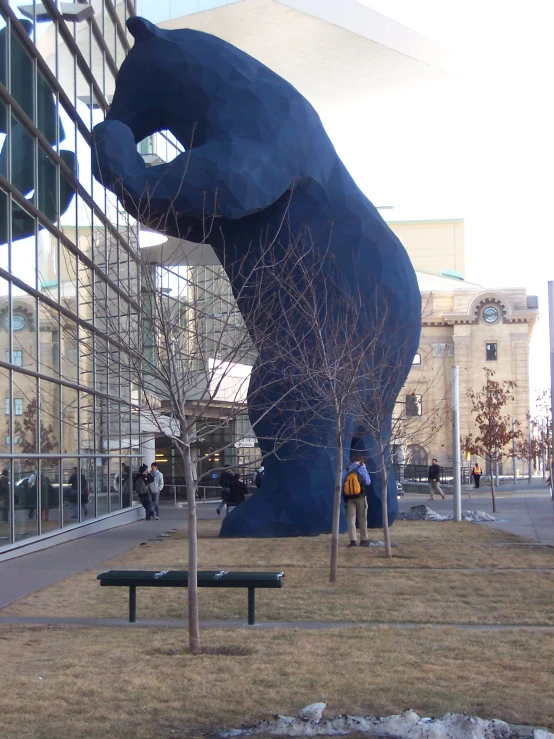 there are two people standing near a large bear statue