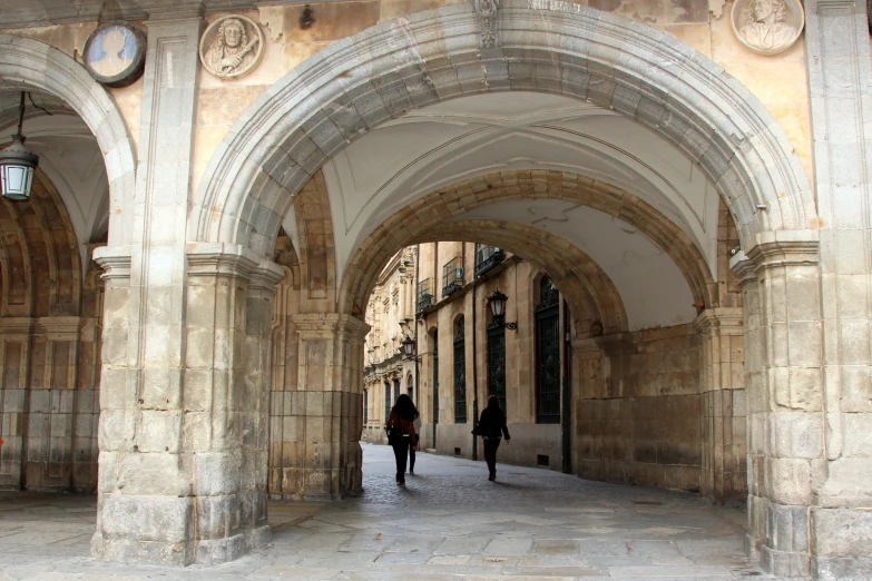 two people walking through an arched stone passage