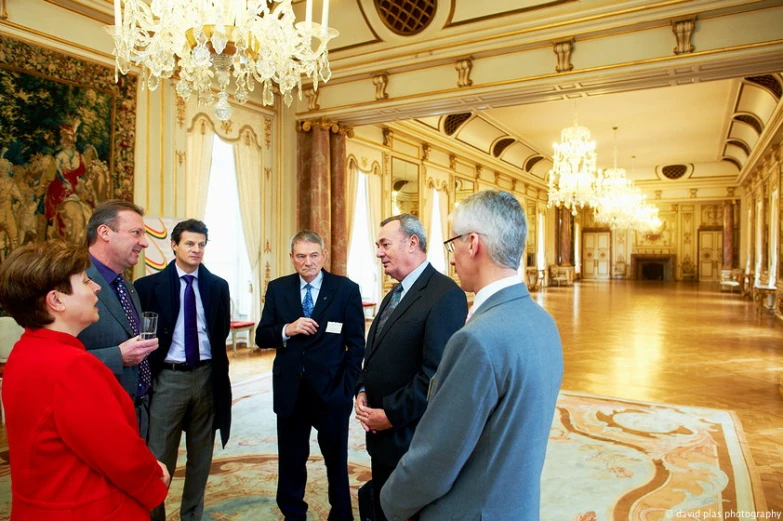 several men and woman dressed in business suits talking in a fancy ballroom