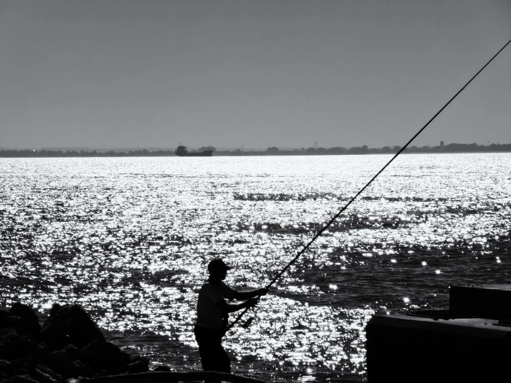 a man fishing on the ocean, with a boat in the background