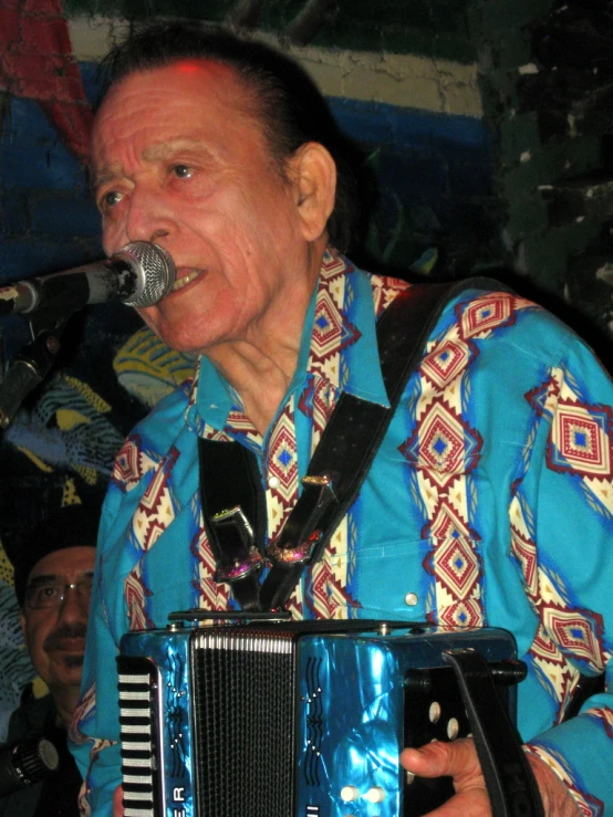 a man in blue with an accordion is singing into a microphone