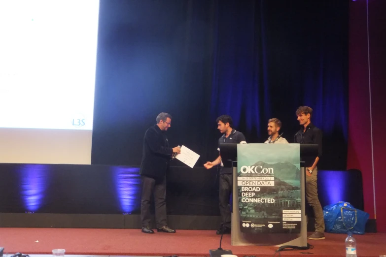 three men standing at podium in front of a projector screen