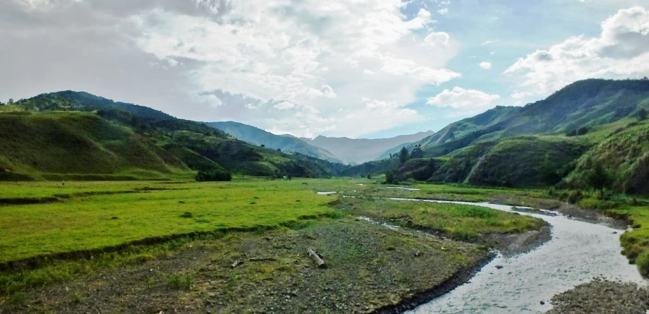 river running through green grassy mountain valley surrounded by tall mountains