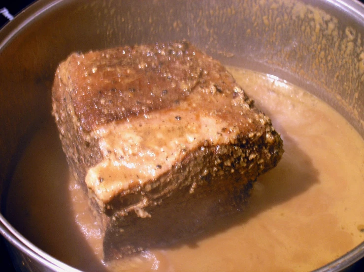 a piece of meat in a pot with some brown oil on it