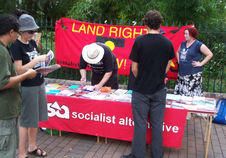 three people standing at a table looking at a red sign