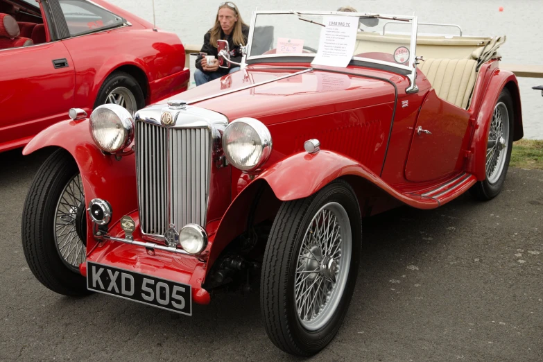 an old fashioned red vintage car sitting parked next to a woman