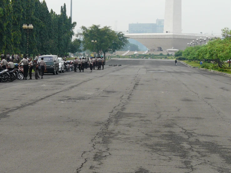 a group of people stand in front of a bunch of parked cars on a road