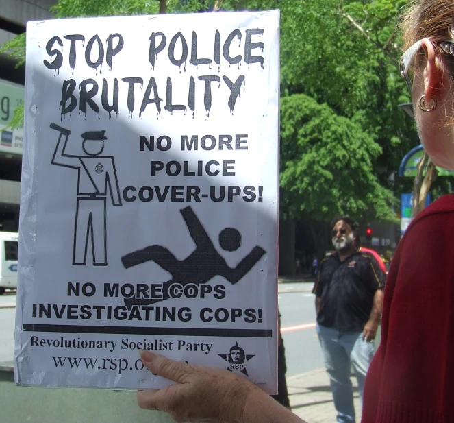 woman holding up sign that warns people not to police over cover