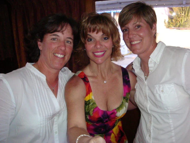 three women pose for the camera in front of a window