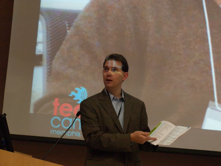 a man wearing glasses at a podium with a book in his hand