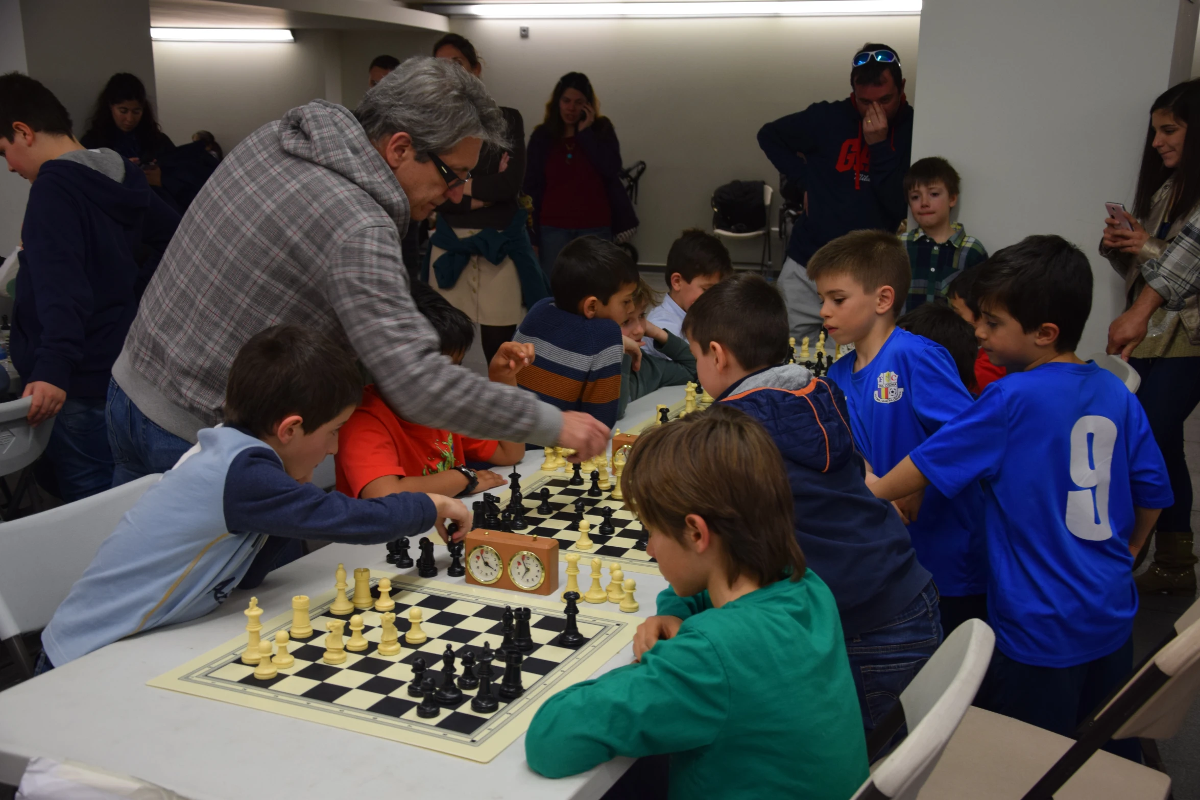 several young children are playing chess while adults look on