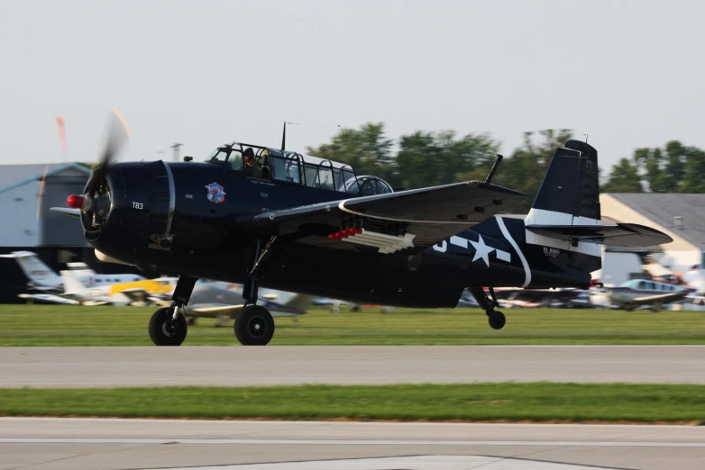 a propeller plane landing at an airport with several other planes on the ground