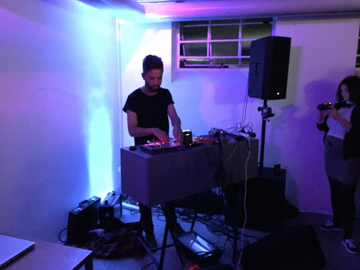 two people standing and sitting around a room with a dj mixer