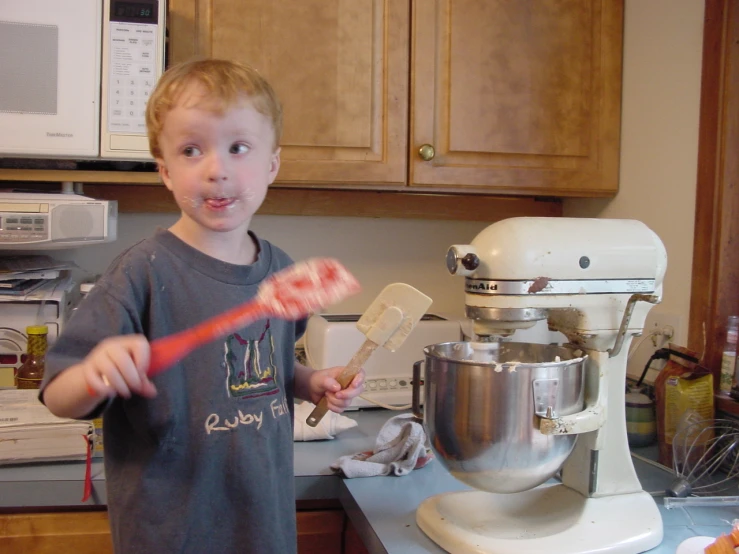 a boy holding a fork in his hand while looking at a mixer