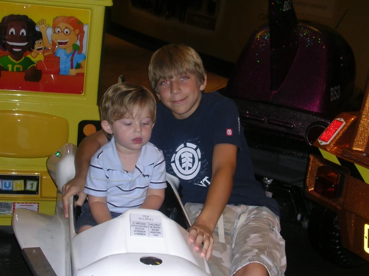 two children are sitting on a miniature toy car