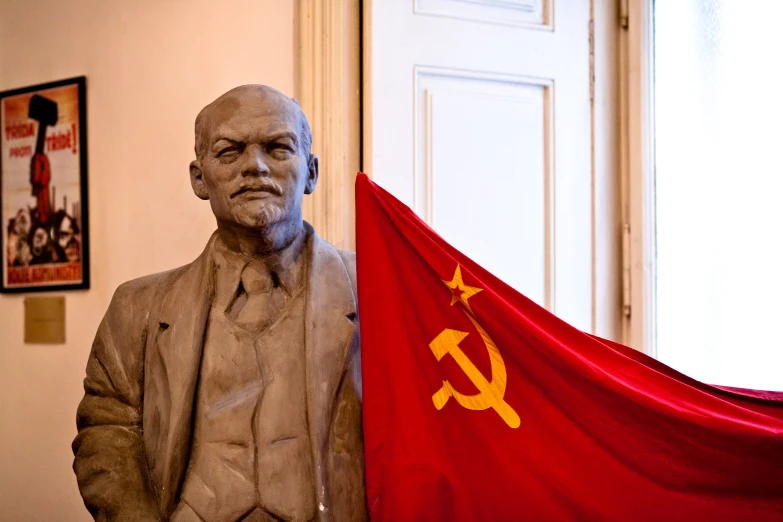 a statue of stalin stands in front of a communist flag