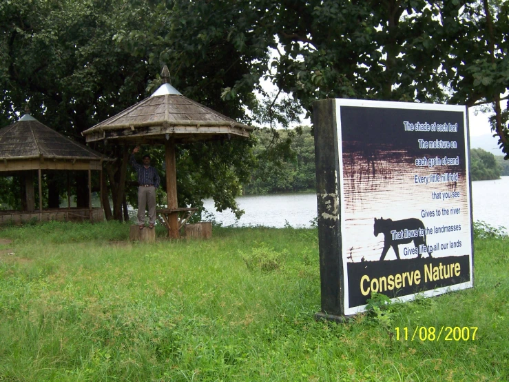 a sign is sitting in front of an umbrella pavilion and body of water