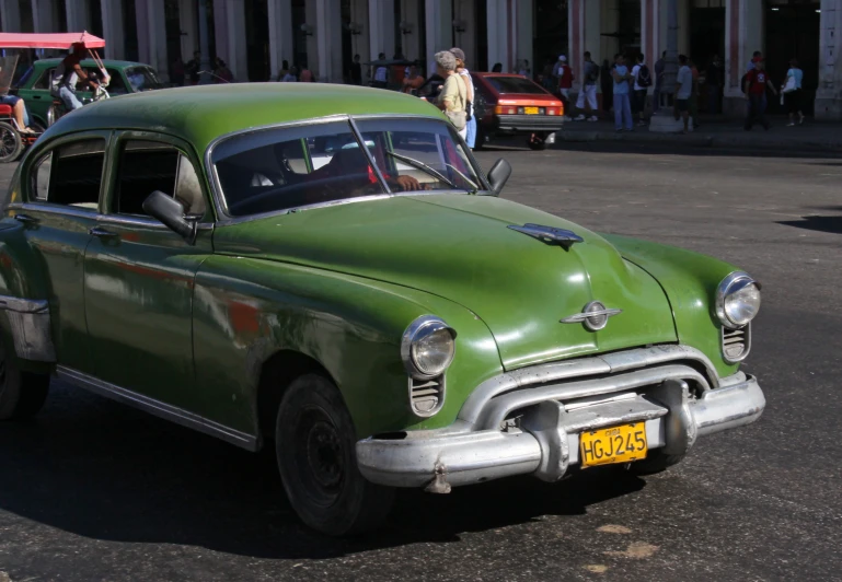 an old fashioned green car parked in front of a crowd of people