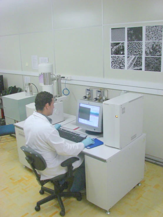 a man in white coat sitting at desk with monitor and printer