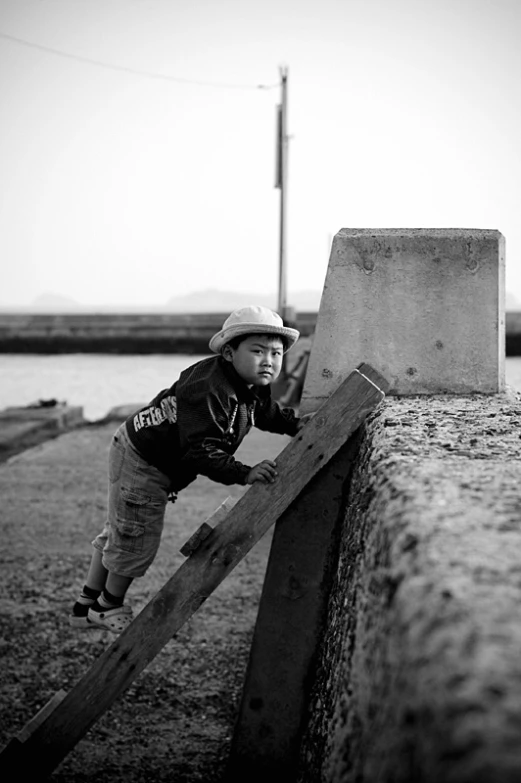 a boy leaning on a wooden rail with his hat over his head