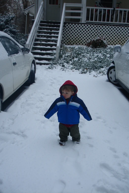 a small child plays in the snow beside some cars