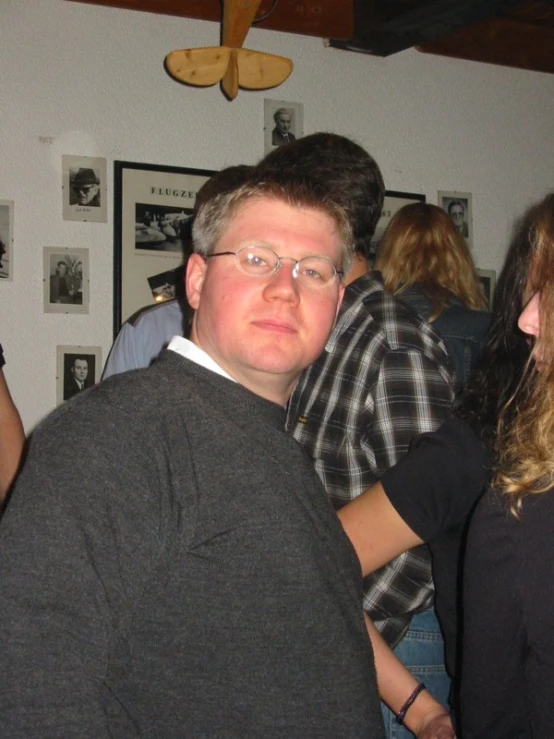 a man wearing glasses and a black top standing in a crowded room