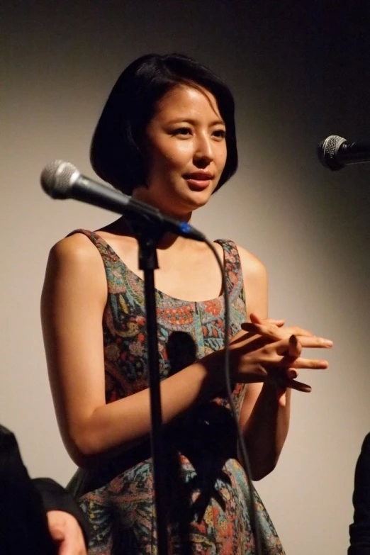 a young asian woman stands at a microphone