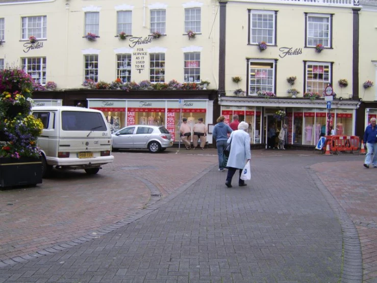 two people in jackets stand in front of shops in a street