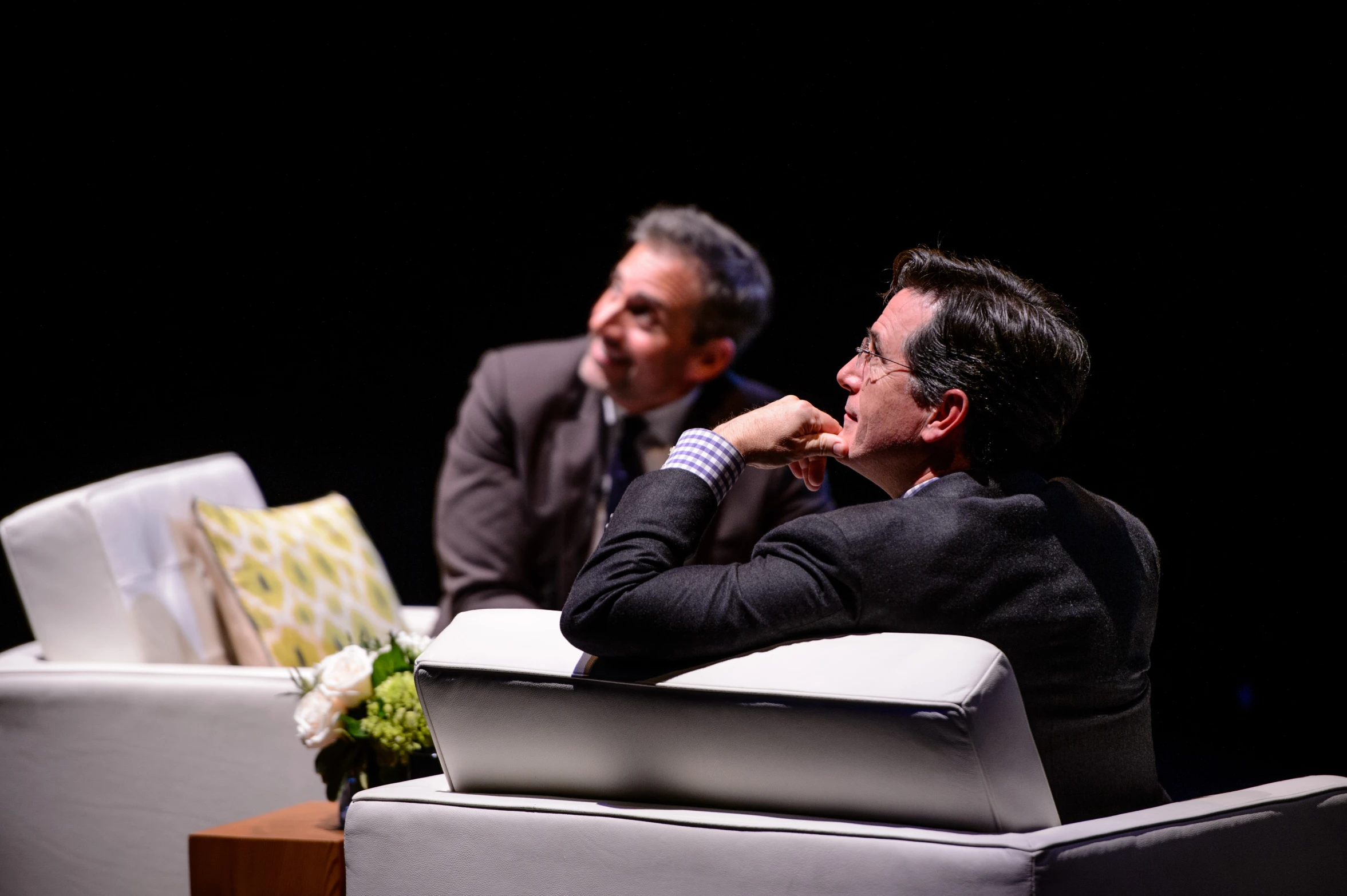 two men sitting next to each other in a black room