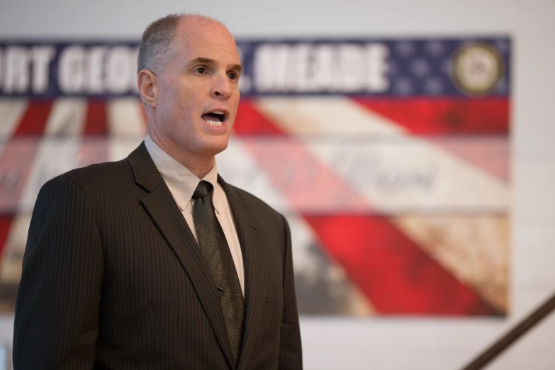 a man with an american flag background giving a speech