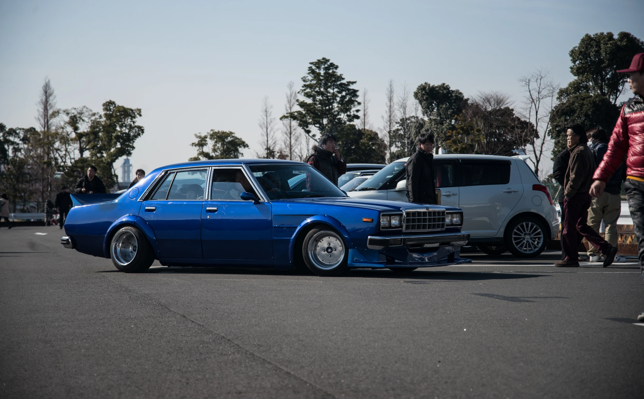 a blue car is on the road with a group of people watching